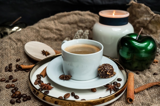 Uma composição estética de uma xícara de café preto com espuma e uma vela acesa, decorada com cho