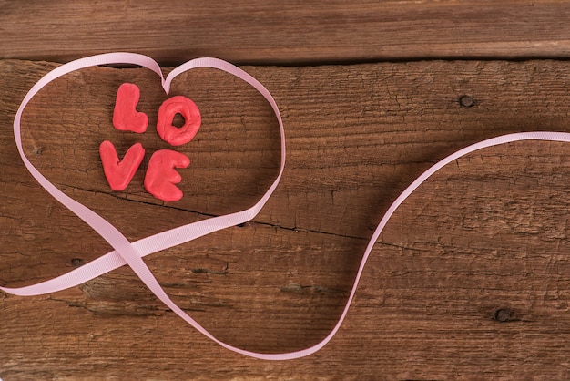 Foto uma confissão de amor na forma de letras de plastilina rodeada por uma fita rosa suave sobre uma superfície de madeira. vista do topo. confissão romântica de amor.