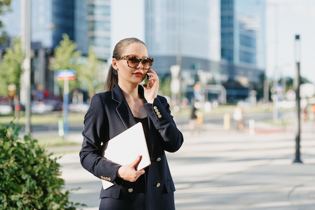 Uma corretora de imóveis feminina de blazer está segurando um laptop no distrito financeiro