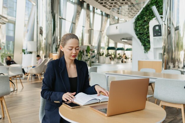 Uma corretora de imóveis feminina de blazer está trabalhando à mesa no lobby moderno