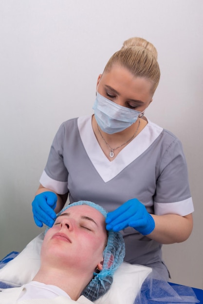 Uma cosmetologista feminina trata manualmente a pele do paciente com um gel hidratante e tonificante