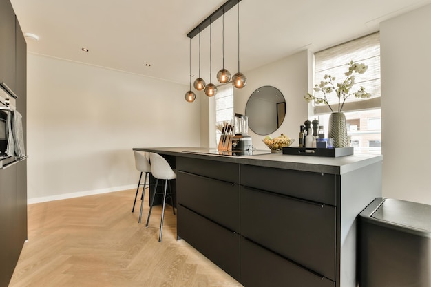 Foto uma cozinha e sala de jantar em uma casa moderna com piso de madeira, paredes brancas, armários pretos e luminárias