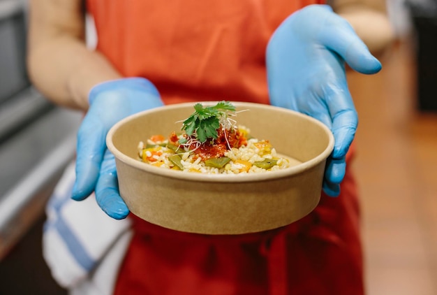 Foto uma cozinheira apresenta sua salada de arroz gourmet em um recipiente compostável para levar