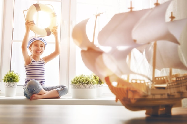 Foto uma criança adorável sentada na janela uma menina sonha com aventuras no mar e viagens uma menina tem um navio de brinquedo