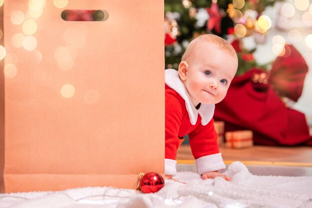 Uma criança alegre com fantasia de Papai Noel olha por trás de uma grande sacola artesanal para receber presentes no fundo de uma árvore de Natal