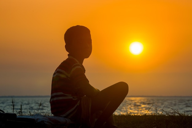 Uma criança aleijada sentada à beira do rio vendo o pôr do sol Um dia terminando Triste história