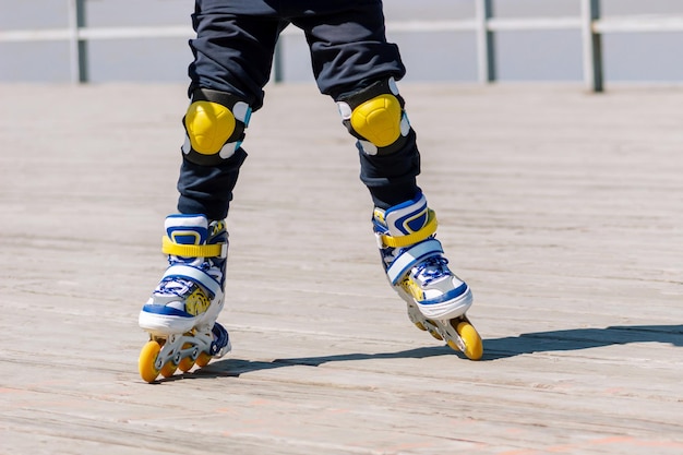 Uma criança anda de patins azuis amarelos e brancos no cais de madeira do mar