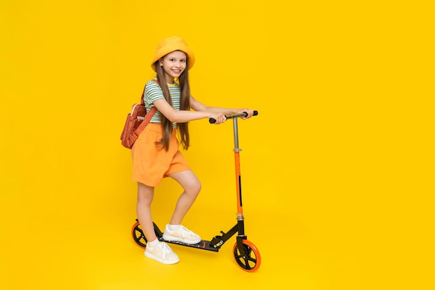 Uma criança anda de scooter Uma vista lateral em comprimento de uma bela menina sonhadora alegre fundo amarelo brilhante isolado