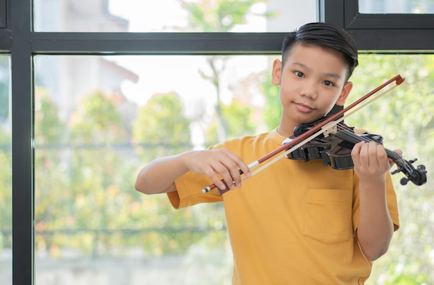 Uma criança asiática tocando e praticando instrumento de cordas musicais de violino contra em casa