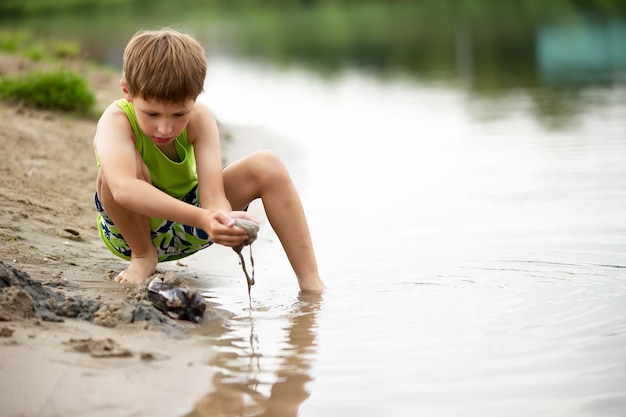 Uma criança brinca com a areia no litoral Um menino na água do lago