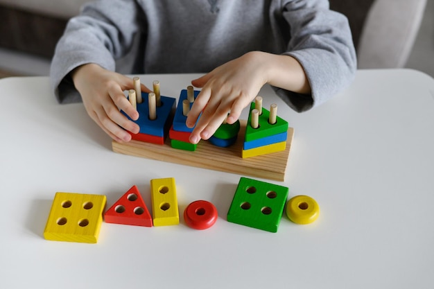 Uma criança brinca com um brinquedo de madeira educacional colorido em casaCloseup