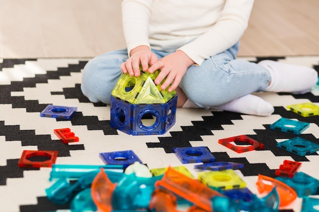 Uma criança brinca com um construtor magnético em um tapete em casa ou no jardim de infância Construindo uma casa de brinquedos com blocos Mãos fechadas