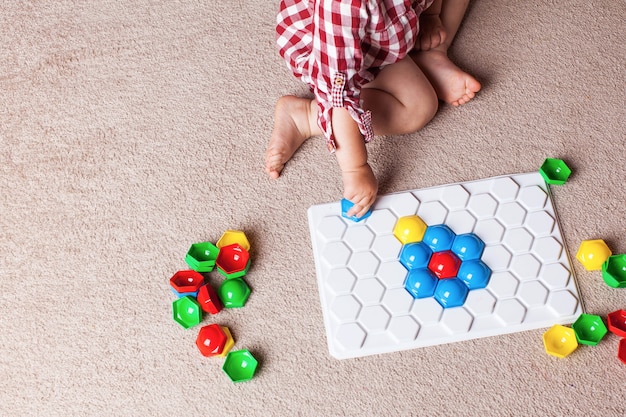 Uma criança brinca com um mosaico de plástico no tapete do quarto das crianças. desenvolvimento inicial, o método montessori.