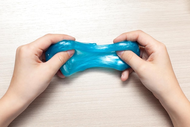 Uma criança brinca com uma mão de lodo azul um antiestresse de brinquedo transparente
