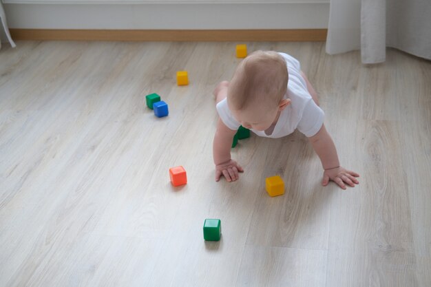 Uma criança brinca no chão com cubos coloridos e constrói uma pirâmide com eles.