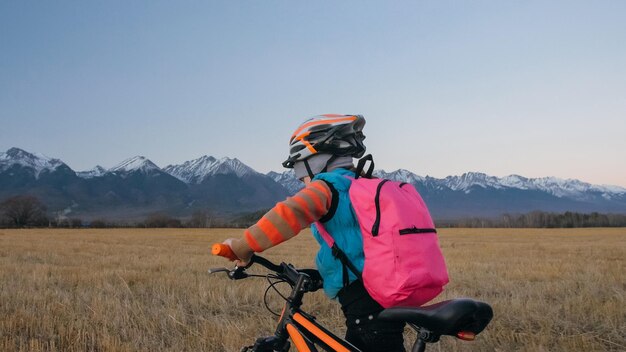 Uma criança caucasiana anda com bicicleta no campo de trigo Menina andando no ciclo laranja preto