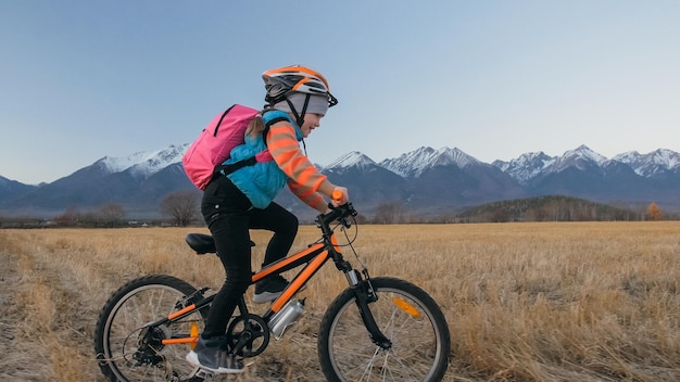 Uma criança caucasiana anda de bicicleta no campo de trigo Menina andando de bicicleta laranja preta no fundo