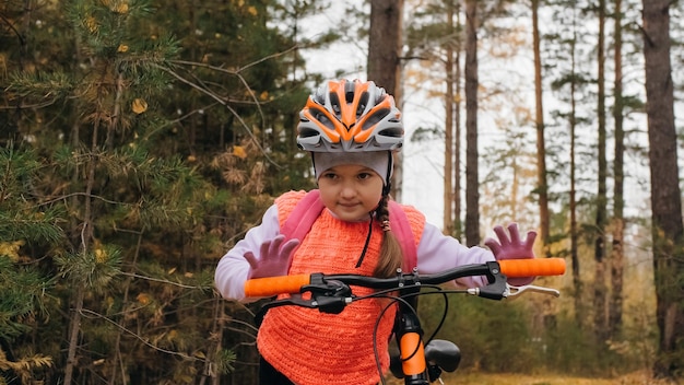 Uma criança caucasiana anda de bicicleta no parque de outono Menina andando em ciclo laranja preto