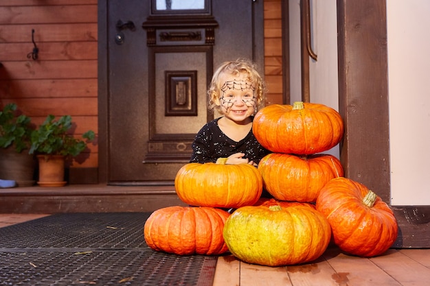 Uma criança celebra o Halloween. A varanda e a porta da frente da casa são decoradas com abóboras. Decoração de halloween