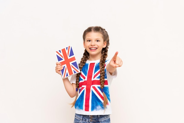 Uma criança com a bandeira da Grã-Bretanha em seu futebol segura um livro sobre a língua inglesa Aprendendo inglês para crianças