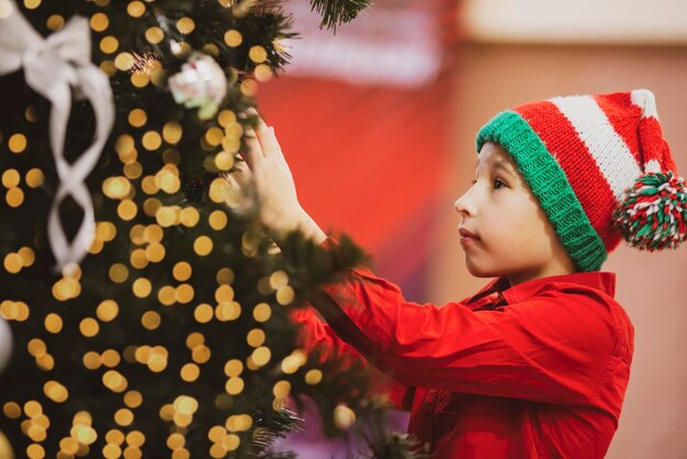 Foto uma criança com um chapéu de natal de malha decora a árvore de natal