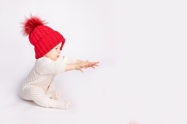 Uma criança com um chapéu vermelho estende os braços sobre um fundo branco e isolado