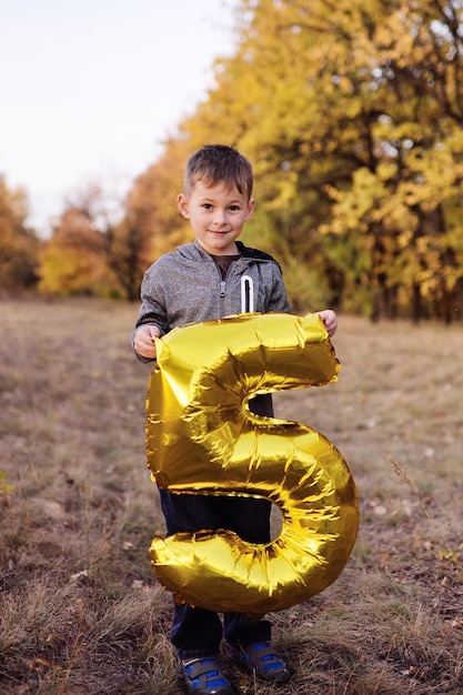 Uma criança com um grande balão em forma de número cinco no fundo da floresta de outono.