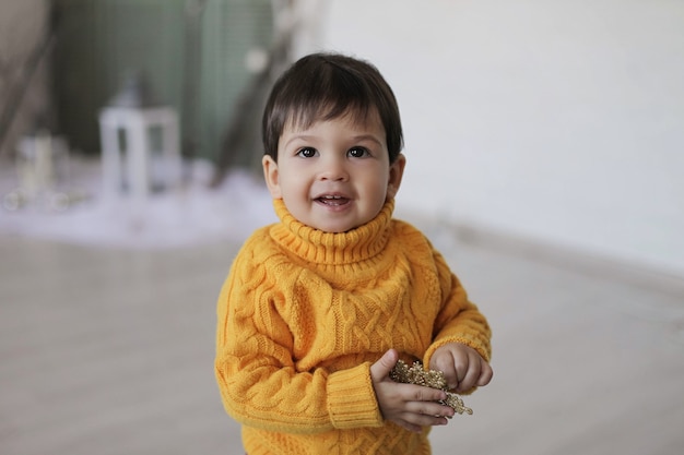 Uma criança com um suéter amarelo segura uma estrela dourada de natal nas mãos e sorri.