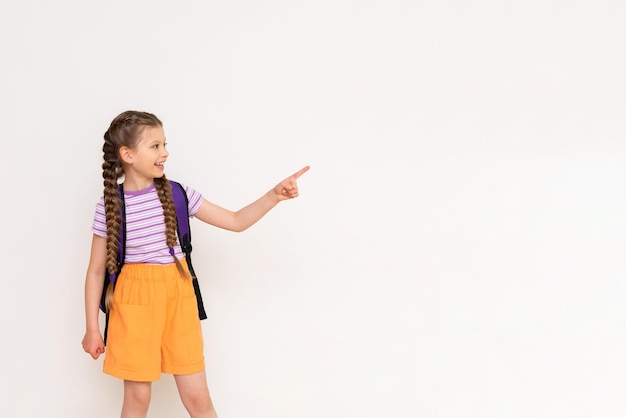 Uma criança com uma bolsa aponta com o dedo indicador para seu anúncio em um fundo branco e isolado cursos preparatórios de verão para crianças espaço para texto