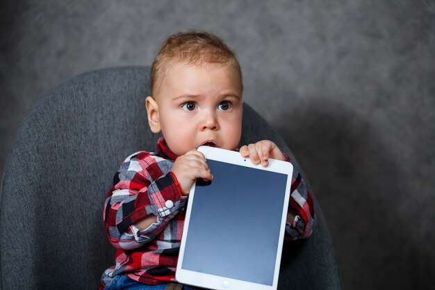 Uma criança com uma camisa mastiga um tablet