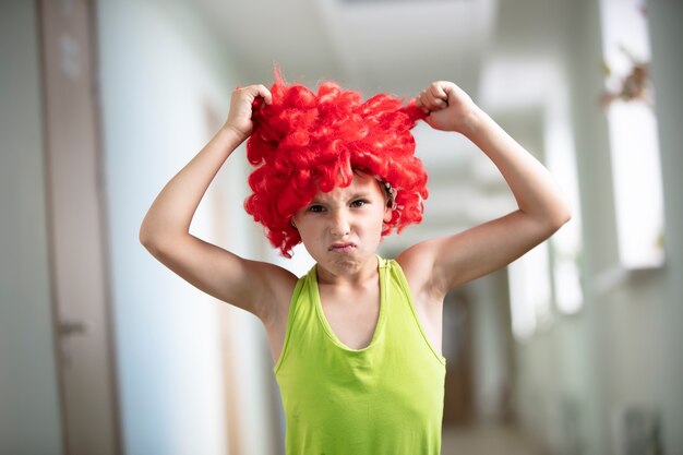 Uma criança com uma peruca brilhante. Engraçadinho com cabelo vermelho artificial.