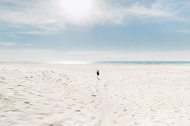 Uma criança corre ao longo de uma praia branca até o mar Báltico em tempo ensolarado. Uma menina corre pela areia branca como a neve para encontrar o mar.