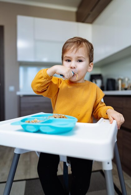 Uma criança curiosa explorando novos sabores Um menino sentado em uma cadeira alta comendo comida