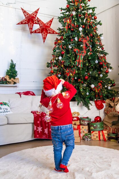 Uma criança dança perto de uma árvore de Natal com uma guirlanda Foco seletivo