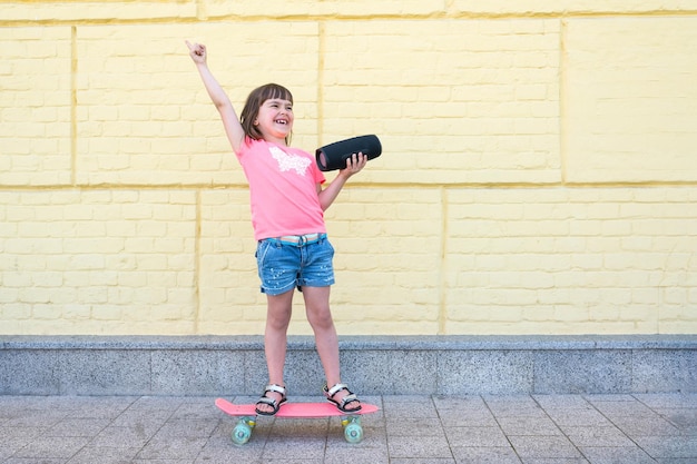 Uma criança de 6 anos anda de skate com uma caixa de som na rua. Estilo de vida ativo