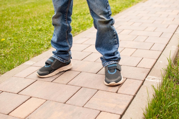 Uma criança de jeans com joelhos sujos de tênis está em pé na calçada