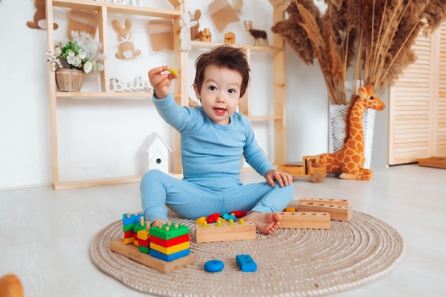 Uma criança de pijama está sentada no chão em seu quarto e brincando com um kit de construção de madeira brinquedos naturais para crianças o menino está brincando em seu quarto