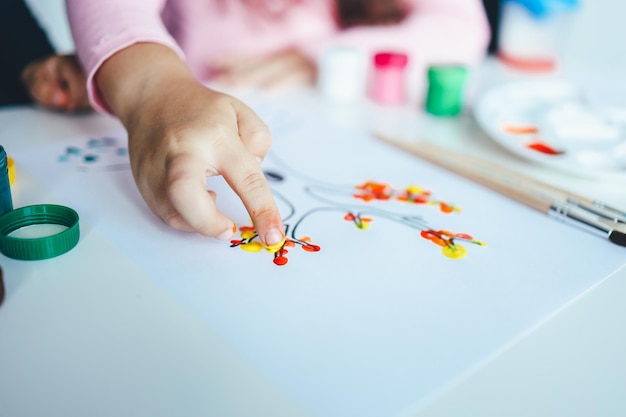 Uma criança desenha folhas em uma árvore Idéias para desenhar com tintas a dedo Pintura a dedo para crianças em fundo branco Menina pintando pela cor da pintura da mão do dedo Conceito de desenvolvimento infantil