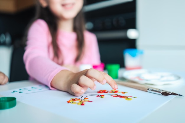 Uma criança desenha folhas em uma árvore Idéias para desenhar com tintas a dedo Pintura a dedo para crianças em fundo branco Menina pintando pela cor da pintura da mão do dedo Conceito de desenvolvimento infantil