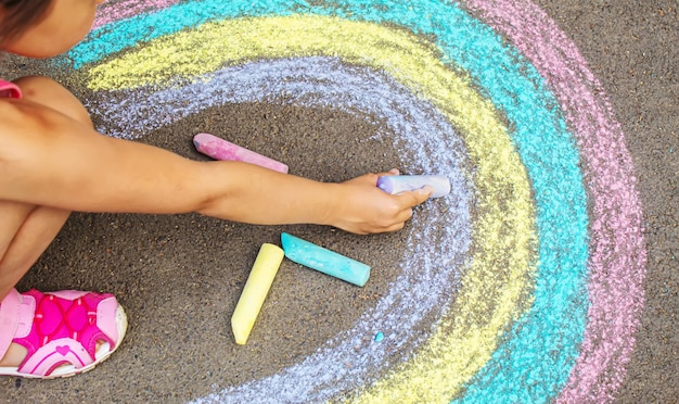 Uma criança desenha um arco-íris no asfalto. Foco seletivo. criança.