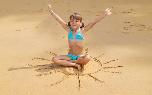 Uma criança desenha um sol na praia.