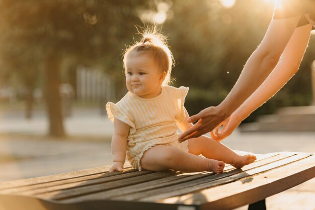 Uma criança do sexo feminino no banco perto de uma mão de uma mãe no parque nas luzes do sol