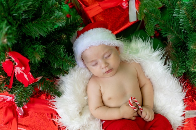 Uma criança dormindo em uma fantasia de papai noel encontra-se com um doce nas mãos em um verde