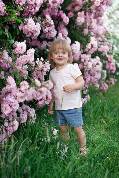 Uma criança é uma menina de vestido branco contra um fundo de roseiras cor de rosa