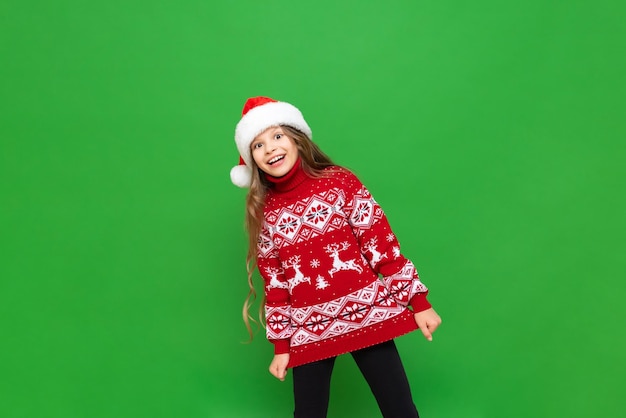 Uma criança em roupas de Natal Linda garotinha com cabelo comprido em um suéter de rena e chapéus de Papai Noel em um fundo verde isolado