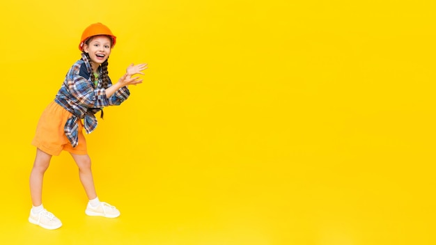 Uma criança em um capacete de construção aponta para o seu anúncio Uma adolescente feliz em plena altura Um lugar para anunciar Fundo amarelo isolado Copiar espaço Banner