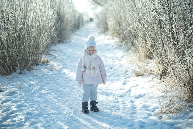 Foto uma criança em um chapéu branco quente e cachecol brinca com neve enquanto caminha na floresta de inverno queda de neve magia de inverno emoção brilhante protegendo a pele da geada