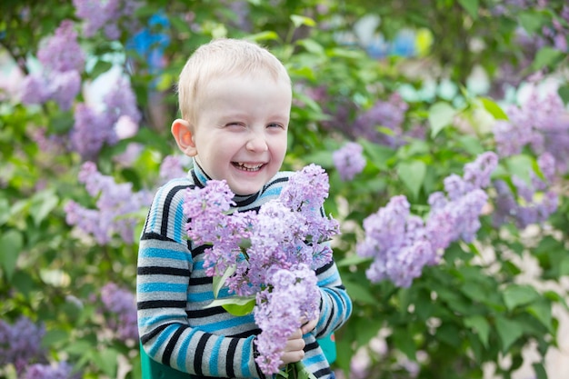 Uma criança em um menino engraçado lilás com um buquê de flores da primavera