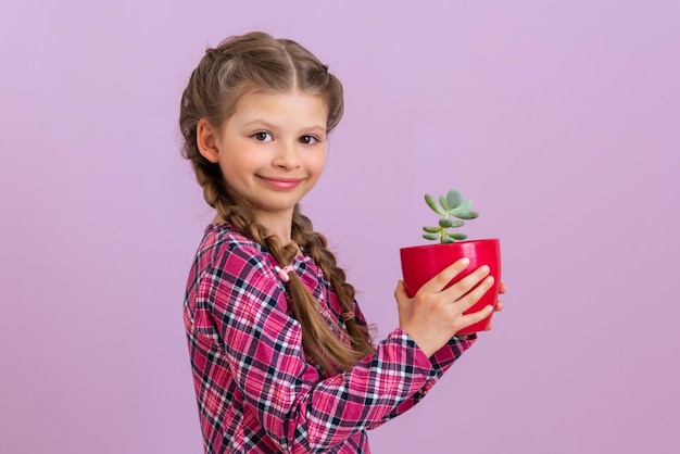 Uma criança em um vestido roxo quadriculado segura uma planta verde em um pote vermelho