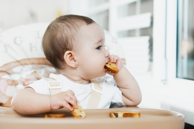 Uma criança em uma cadeira alta comendo um biscoito com passas